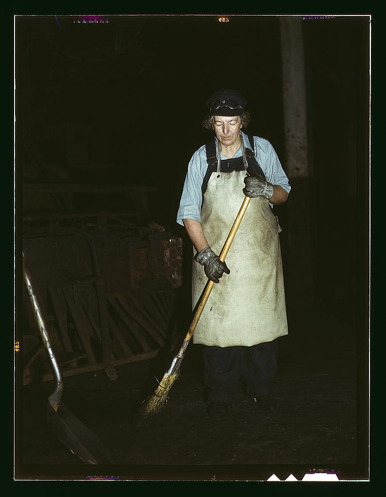 A woman in an apron sweeps in front of a dark background.