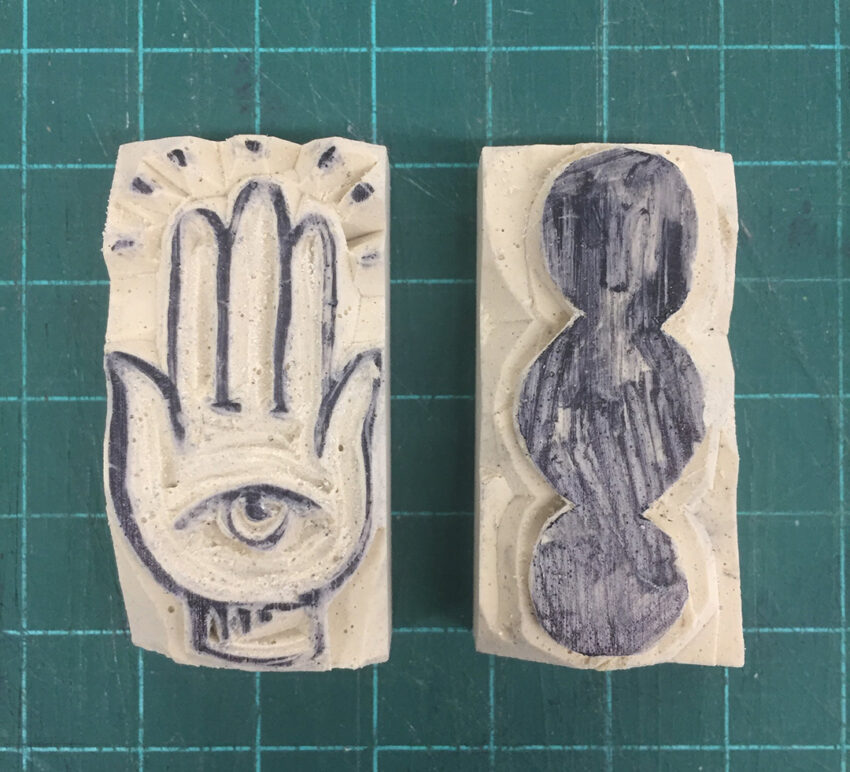 An image of two small erasers carved for relief printing. One eraser shows the hamsa, a symbol with an eye in a hand. The other eraser shows three circles touching.