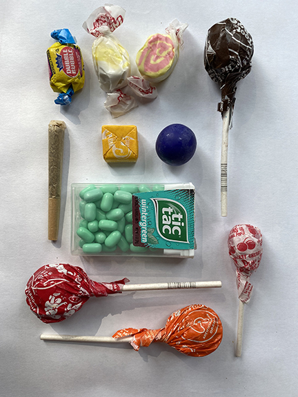 An orderly collection of suckers, tic-tacs, what looks like a joint but is a fancy rolled cigarette, and some candies.