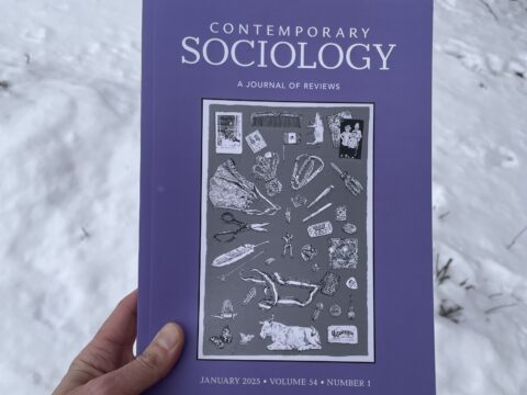 An image of a white hand holding a print copy of the journal "Contemporary Sociology." The cover of the journal features a black and white image of a print by Katie Ries. The print is a line drawing of several small objects.